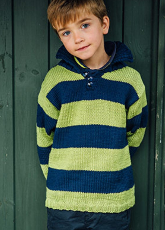 Taylor Sweater: Child wearing a hand-knitted sweater with horizontal dark blue and light green stripes, standing in front of dark green wooden panels.
