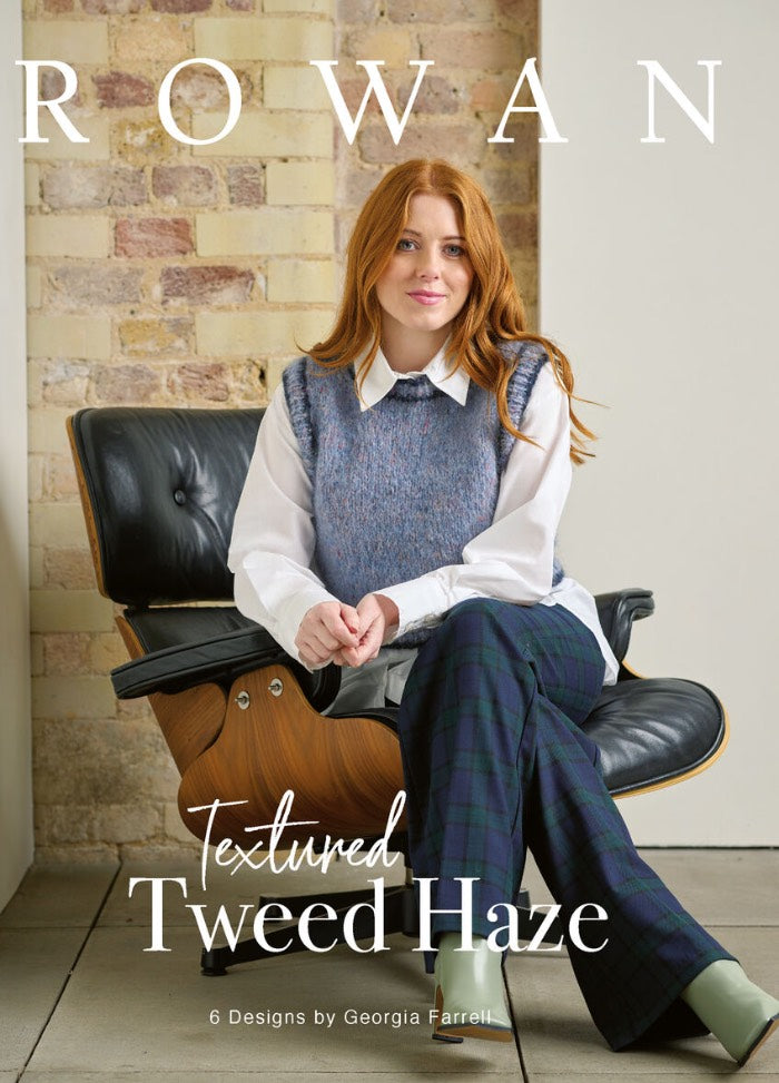 Woman with long red hair sits on a black chair, wearing a blue sweater vest and plaid pants. Background features a brick wall. Text reads "Rowan, Textured Tweed Haze."
