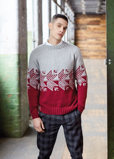 Young man in a cozy red and gray patterned sweater stands in an industrial-style hallway with brick walls and wooden accents, exuding a relaxed vibe.