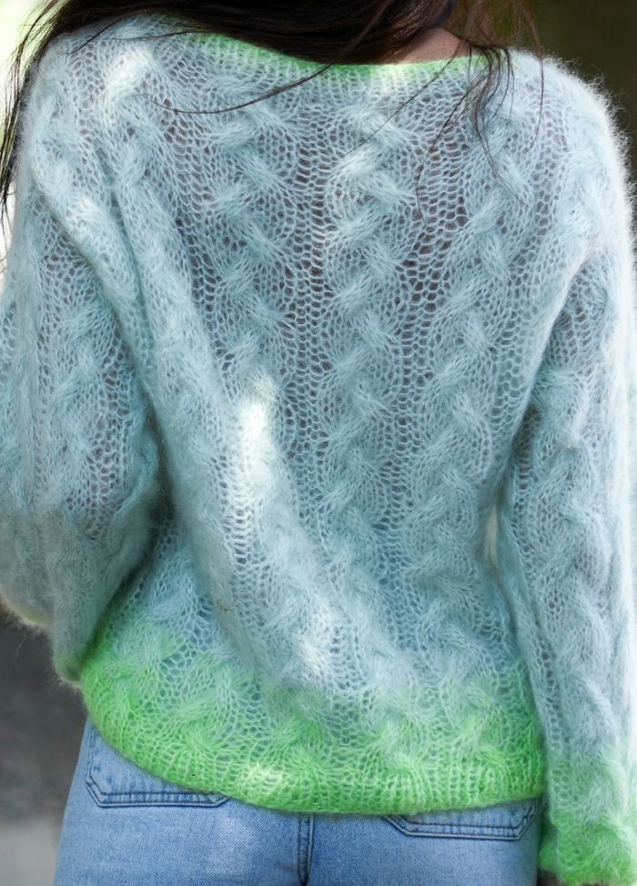A person wearing a soft, translucent blue sweater with green gradient detail at the hem, paired with blue jeans. The scene is calm and casual.