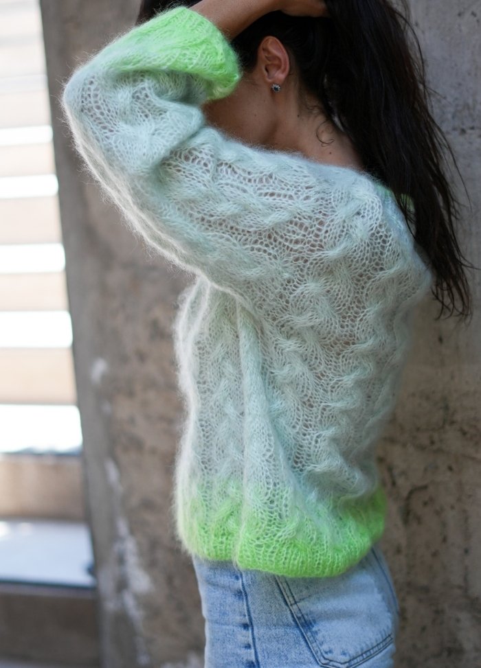 A person wearing a soft, translucent blue sweater with green gradient detail at the hem, paired with blue jeans. The scene is calm and casual.