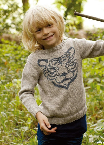 Child in light gray Tiger Sweater with tiger face motif, outdoors with plants.