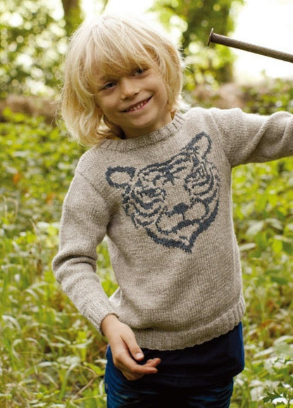 Child in light gray Tiger Sweater with tiger face motif, outdoors with plants.