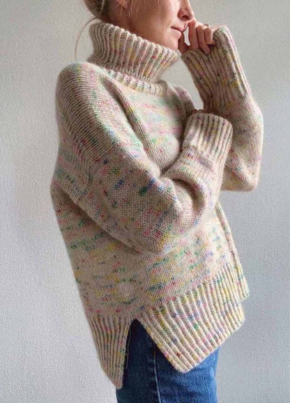 Woman in a cozy, speckled knit turtleneck sweater with loose sleeves, standing sideways in a relaxed pose, conveying warmth and comfort.