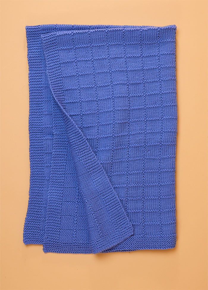 Window Pane Blanket in soft blue, featuring a textured grid of small square panels laid flat to showcase its geometric knit design.