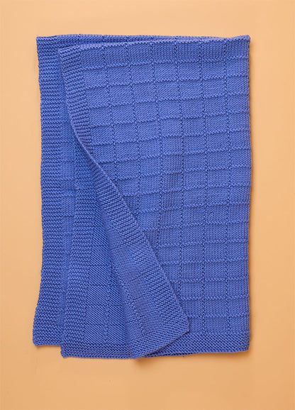 Window Pane Blanket in soft blue, featuring a textured grid of small square panels laid flat to showcase its geometric knit design.