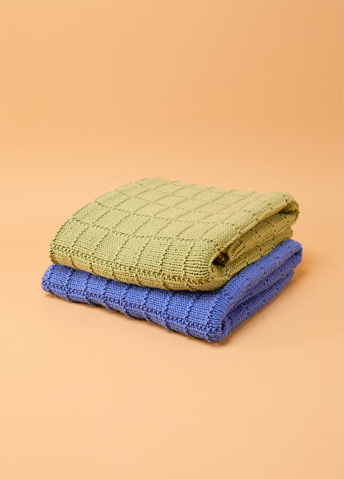 Two folded Window Pane Blankets in green and blue, stacked against a beige background, each featuring a textured square panel design.