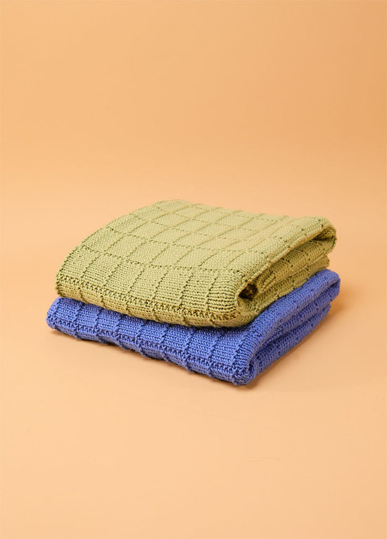 Two folded Window Pane Blankets in green and blue, stacked against a beige background, each featuring a textured square panel design.