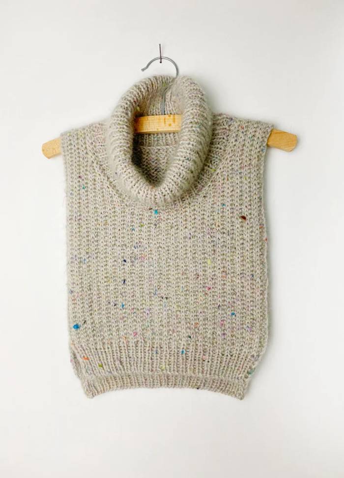 Grey knitted neckwarmer with a turtleneck on a wooden hanger, featuring multicoloured speckles, against a plain white background. Cozy and neutral tone.