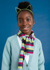 Smiling child wearing a cat ear headband, colorful striped scarf, and light blue cardigan against a blue background, conveying warmth and joy.