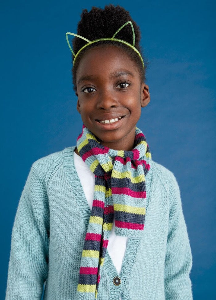 Smiling child wearing a cat ear headband, colorful striped scarf, and light blue cardigan against a blue background, conveying warmth and joy.